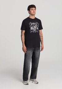 Czarna bawełniana koszulka z białą grafiką motocykla. W połączeniu z ciemnoszarymi dżinsami i szarymi sneakerami. Prosty, casualowy design.