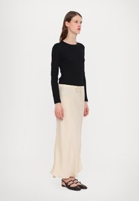 Black long-sleeve top, cream-colored maxi skirt with drawstring waist, smooth fabric, and brown shoes with straps and round accents.