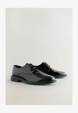 Mustad mustad nahast kingad läikiva viimistlusega, ümarate varvaste ja nööpidega disainiga. Paks tall, millel on nähtavad õmblused ja minimaalne aktsent.