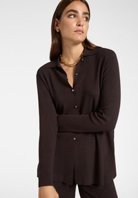 Zwarte button-up cardigan met lange mouwen, gemaakt van soepel stof. Heeft een kraag en subtiele knoopaccenten.