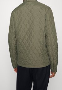 Gestepptes olivgrünes Jacket mit Stehkragen, Druckknopfverschluss am Handgelenk und durchgehendem Rautenmuster.