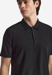 Svart polo skjorta i lättviktig tyg, med krage och platta med tre knappar. Korta ärmar med en mjuk textur, utan mönster.