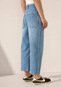 Jeans de mezclilla a rayas azul claro con cintura alta, pierna ancha y bolsillos traseros, combinados con zapatillas marrones y blancas.