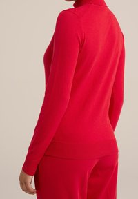 Pull à col roulé rouge en tissu doux. Design ajusté avec des poignets et un ourlet côtelés. Texture lisse, vue de l'arrière.