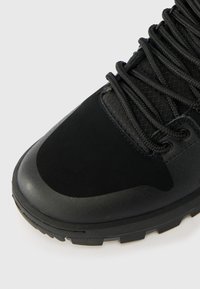 Μαύρο, υφασμένο αθλητικό παπούτσι με λείο προστατευτικό καπάκι, πλεκτούς κορδόνες και ανθεκτική σχεδίαση σόλας με αυλάκια.