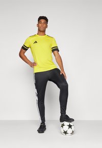 Yellow athletic t-shirt with black accents and stripes, paired with black pants featuring white side stripes, complemented by a soccer ball.