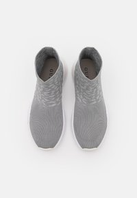 Szare sneakersy wsuwane, wykonane z materiału o fakturze dzianinowej; mają białą podeszwę i wzorzyste detale w górnej części.