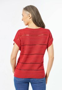 Rode gebreide top met korte mouwen, voorzien van een textuurpatroon met horizontale strepen en kleine uitsparingen, gecombineerd met blauwe jeans.