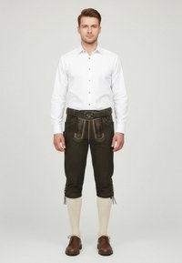 Bruna läderlederhosen med dekorativ sömnad, bärs med en vit skjorta, elfenbensfärgade knä-långa strumpor och bruna skor.