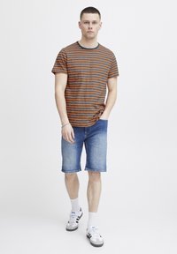Striped short-sleeve t-shirt in orange and navy, paired with denim shorts. Model wearing white socks and grey sneakers with black accents.