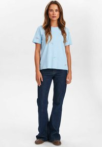 Camiseta de manga corta azul claro con bordado floral, combinada con jeans acampanados azul oscuro y zapatos marrones, con un ajuste relajado.