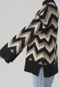 Sweter dzianinowy w czarno-brązowo-kremowy wzór w zygzaki, z prążkowanym dekoltem i oversize'owymi rękawami, oraz bocznymi rozcięciami u dołu.