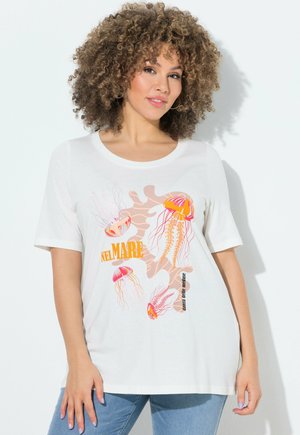 Frau mit lockigem Haar, die ein weißes T-Shirt mit bunten Quallen und orangefarbenem Text "NEL MARE" trägt und vor einem weißen Hintergrund steht.