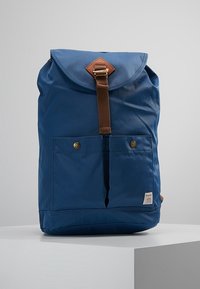 Zaino in tessuto blu con chiusura a patta, tracolla in pelle marrone, tasche frontali e finitura testurizzata. Presenta un piccolo etichetta del marchio nella parte inferiore.