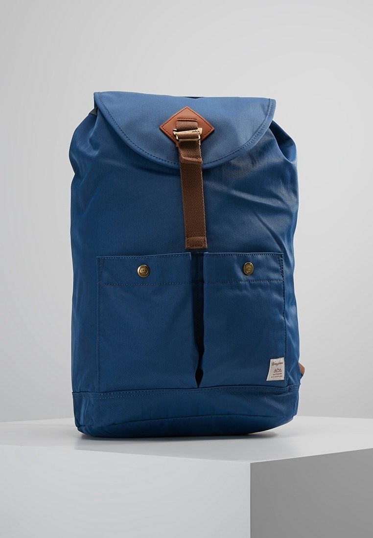 Zaino in tessuto blu con chiusura a patta, tracolla in pelle marrone, tasche frontali e finitura testurizzata. Presenta un piccolo etichetta del marchio nella parte inferiore.