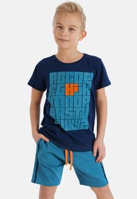 Marineblå T-shirt med stort grafik af teal bogstaver og en orange detalje; parret med teal shorts med en orange snøre og sidelister.