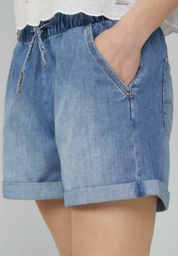 Shorts en denim bleu clair avec une coupe décontractée, dotés d'une taille à cordon de serrage, de poches latérales et de revers.