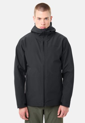 Man draagt een zwarte waterdichte jas met capuchon en rits aan de voorkant, staand tegen een eenvoudige lichte achtergrond.