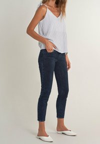 Top senza maniche bianco e blu a righe con scollatura a V, abbinato a jeans skinny blu scuro e scarpe slip-on bianche.