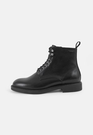 Schwarze Leder-Stiefeletten mit runder Zehenpartie, Schnürverschluss vorne und fester flacher Sohle; verfügen über eine Zugschlaufe an der Rückseite für ein einfaches An- und Ausziehen.