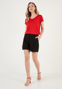 Rød v-hals t-shirt parret med sorte shorts. Outfitten har en afslappet pasform, letvægtsstof og en glat tekstur. Komplementeres med multikolorede hæle.