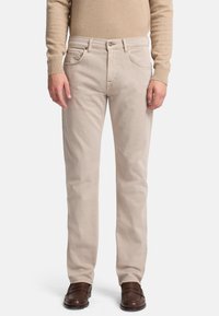 Jeans di denim beige con un design a gamba dritta, cinque tasche e una sottile texture stonewash, abbinati a scarpe in pelle marrone.