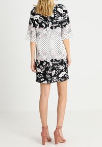 Šaty s květinovým vzorem a černobílými částmi, krátké rukávy a vypasovaný střih. Výrazné růžové květiny a puntíky.