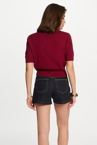 Bordeaux rood kortafgemeten trui met geribbelde kraag, gecombineerd met donkerdenim short met hoge taille, voorzien van dubbele achterzakken en contrasterende stiksels.