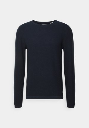 Maglione blu navy a maniche lunghe, colletto tondo, tessuto strutturato, design attillato, con un sottile dettaglio dell'orlo in fondo e un'etichetta sul lato.