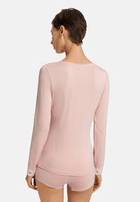 Top de manga larga en color rosa, hecho de un tejido suave, con detalles de encaje en los puños. Combinado con pantalones cortos rosas a juego.