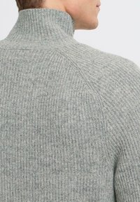 Maglione a costine grigio chiaro con colletto alto e finitura texturizzata, che presenta un design delle spalle senza cuciture.
