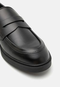 Black leather loafers with a shiny finish, featuring a wide strap design, rounded toe, and a black rubber sole. Smooth texture, minimal stitching.