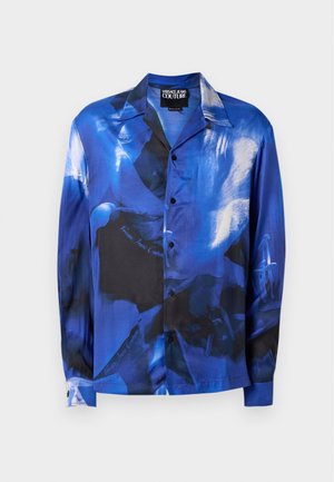 Zilā un melnā krāsā garie piedurknes krekls, ar abstraktiem rakstiem, pogu priekšpusi un apkakli. Izgatavots no gludas, spīdīgas auduma.