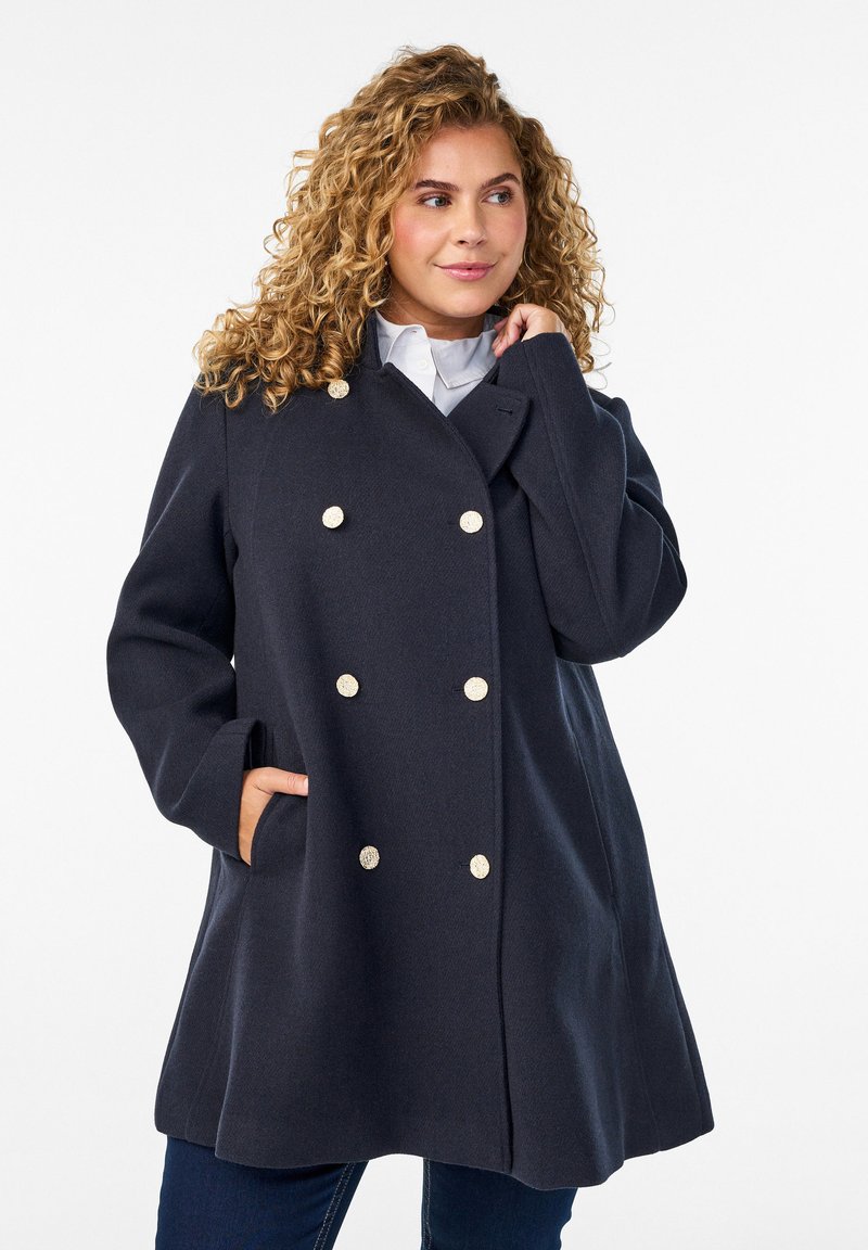 Navy double-breasted coat with gold buttons, featuring a relaxed fit and side pockets. Smooth fabric with a structured design.