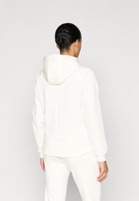 Λευκό φούτερ με κουκούλα από μαλακό υλικό, με μανίκια ράγκλαν, εφαρμοστό τελείωμα και ελάχιστες λεπτομέρειες στην πλάτη.