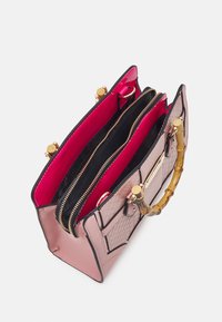 Różowa torebka z bambusowym uchwytem, z pikowaną teksturą, złotymi akcesoriami i kontrastowym czerwonym wnętrzem. Posiada trzy zamykane na zamek przegrody.