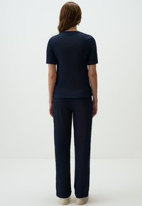 Completo navy in due pezzi composto da una maglietta a maniche corte in maglia testurizzata e pantaloni dritti e larghi, abbinato a sneakers di colore chiaro.