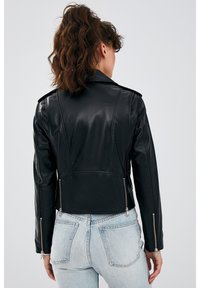 Zwarte leren cropped jack met gestructureerde schouders, zilveren ritsen op de mouwen en een gladde afwerking. Gestyled met lichtblauwe high-waisted jeans.