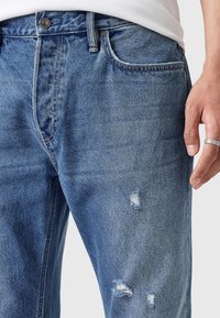 Jasnoniebieskie dżinsy z lekkimi przetarciami, posiadające pięć kieszeni, zapięcie na guzik i zamek błyskawiczny oraz kontrastowe szwy.