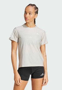 Camiseta atlética de color gris claro con cuello redondo, mangas cortas y tres rayas blancas en el hombro izquierdo, combinada con pantalones cortos negros.