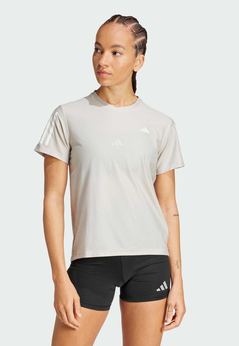 Camiseta atlética de color gris claro con cuello redondo, mangas cortas y tres rayas blancas en el hombro izquierdo, combinada con pantalones cortos negros.