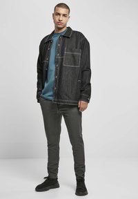Svart denimjakke med hvite sømmer, en brystlomme, kombinert med en turkis t-skjorte og grå slim-fit bukser. Svart sneakers fullfører antrekket.