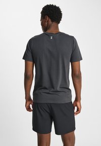 Mörkgrå kortärmad T-shirt, tillverkad av bomull, med rund halsringning och tre vertikala ränder på övre delen av ryggen.