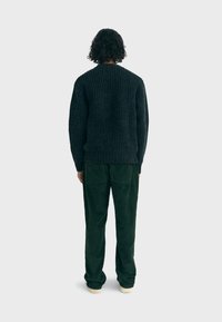 Dark ribbed sweater with dropped shoulders, paired with green corduroy pants featuring side pockets. White sneakers complete the look.