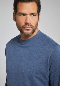 Svetr v tmavě modré pletenině s kulatým výstřihem. Obsahuje jemné logo "JP" na hrudi. Klasický design s hladkým povrchem.