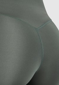 Legíny s vysokým pasem v tlumené zelené barvě, vyrobené z hladkého, elastického materiálu. Obsahují švy s křivkovým prošíváním na zadní straně.