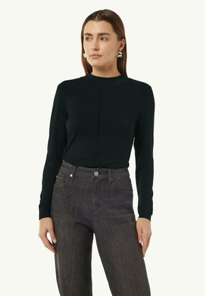 Top nero a maniche lunghe con colletto alto e un sottile dettaglio della cucitura frontale, abbinato a jeans di denim scuri con chiusura a bottoni classica.