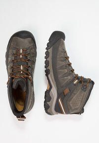 Graue Wanderschuhe mit robustem Design, ausgestattet mit braunen Akzenten, strukturierten Obermaterialien und einer stabilen Gummisohle mit ausgeprägtem Profil.