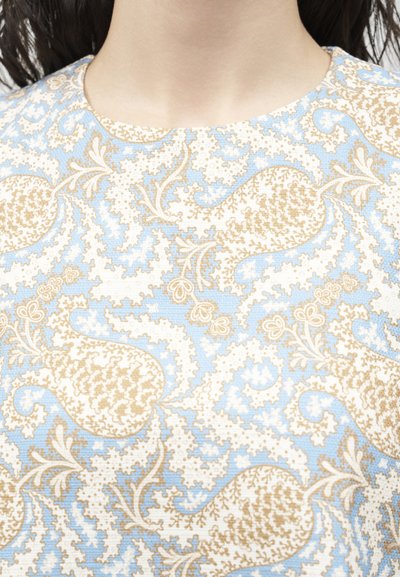 Κοντινή λήψη ενός ατόμου που φοράει πουκάμισο με μοτίβο πασλέ σε ανοιχτό γαλάζιο και μπεζ χρώμα, με στρογγυλή λαιμόκοψη.