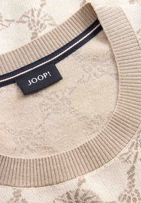 Suéter beige con un patrón floral texturizado, cuello redondo acanalado y una franja de acento azul oscuro. Presenta una etiqueta negra con la palabra "JOOP!".